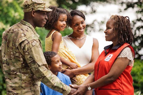 Red Cross volunteer shaking hands with military service member who's next to his family.