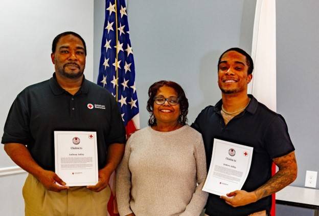 two men and a woman dressed in business casual with men holding framed certificates