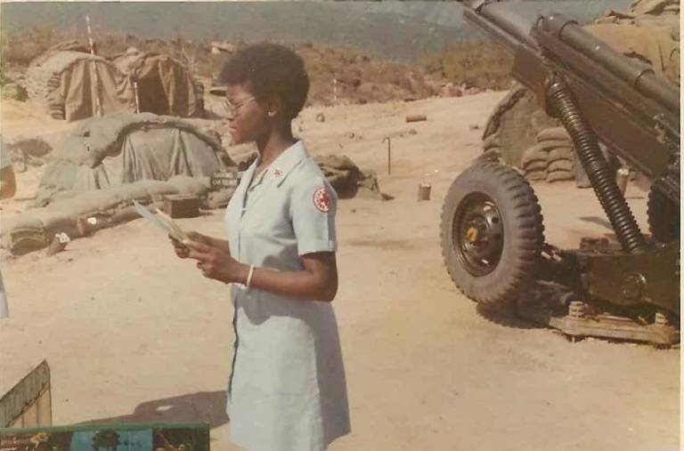 young girl in light blue Red Cross uniform in front of military equipment
