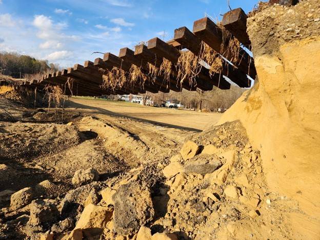wooden railroad tracks hang in the air with the ground underneath washed away in a flood.