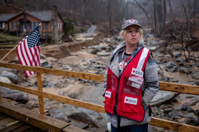 Young woman in winter clothing and a Red Cross vest stands on a bridge.