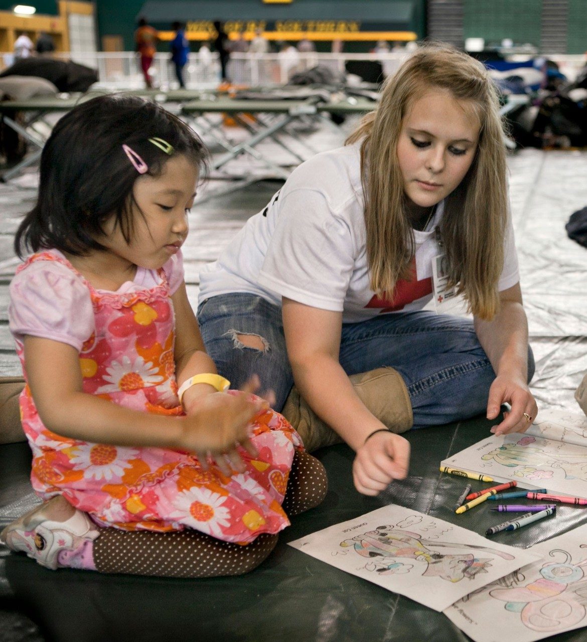 Red Cross volunteer coloring with child.