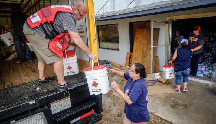 Man in Red Cross vest standing in a box truck and handing a Red Cross bucket to another volunteer.