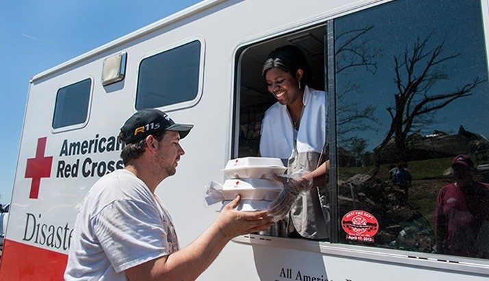 Red Cross volunteer in Red Cross van handing food to man through window.