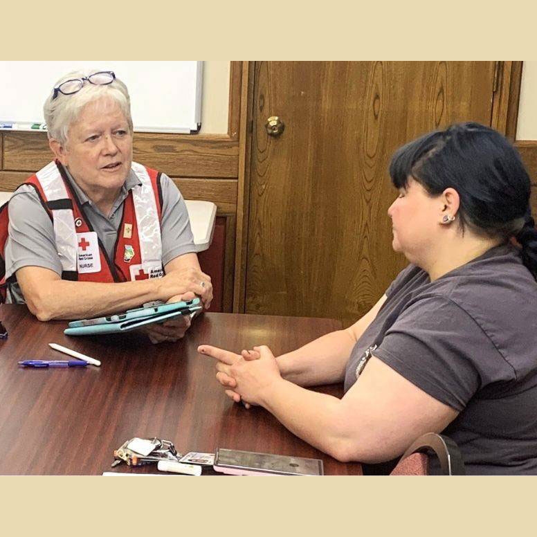 Patsy Alleman speaking with Red Cross volunteer while sitting at a desk.