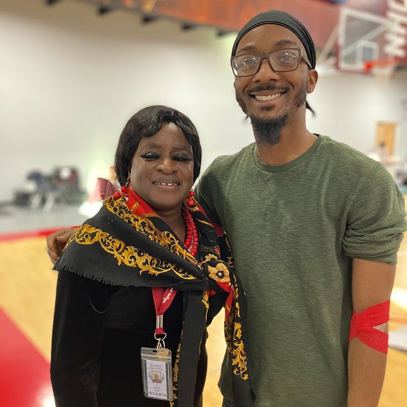 Two black people, one with red bandage around arm, smile for picture.