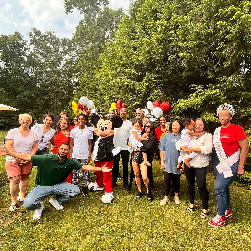 Group photo of a large group of people on grass with Mickey Mouse mascot and balloons.
