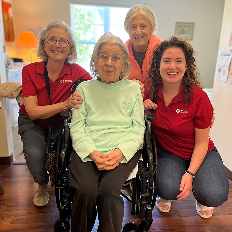 Rita Schmid sitting in wheelchair surrounded by three Red Cross volunteers and all smiling for picture.