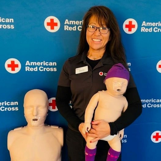 Heather wearing Red Cross shirt, holding manikin and smiling.
