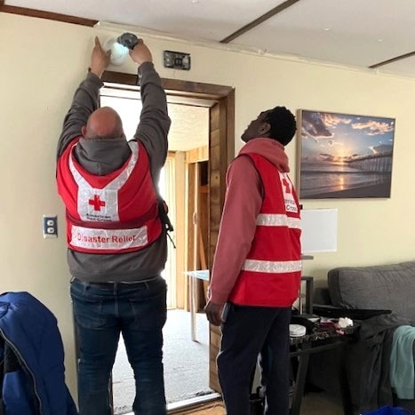 Two Red Cross volunteers install a smoke alarm in a house.
