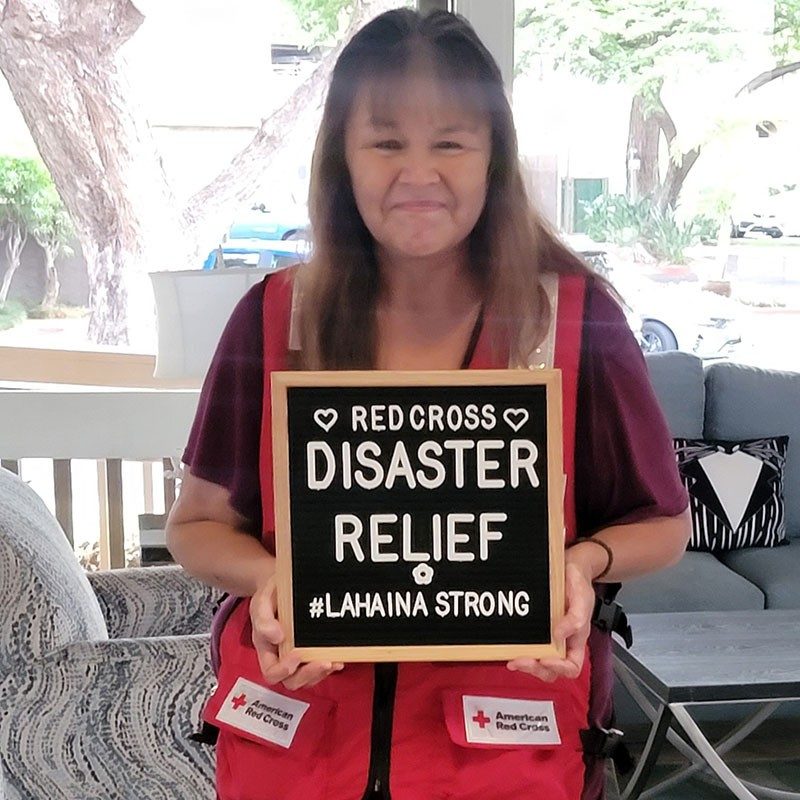 Stephanie Raygoza-Garcia wearing Red Cross vest and holding a sign that says, Red Cross Disaster Relief Lahaina Strong.