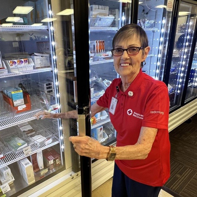 Judy Button wearing a Red Cross shirt and lanyard, opens see-through refrigerator door and smiles for picture.