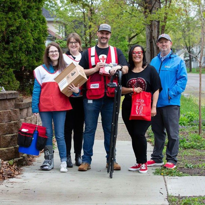 Five Red Cross volunteers walking on sidewalk with gear to install smoke alarms.