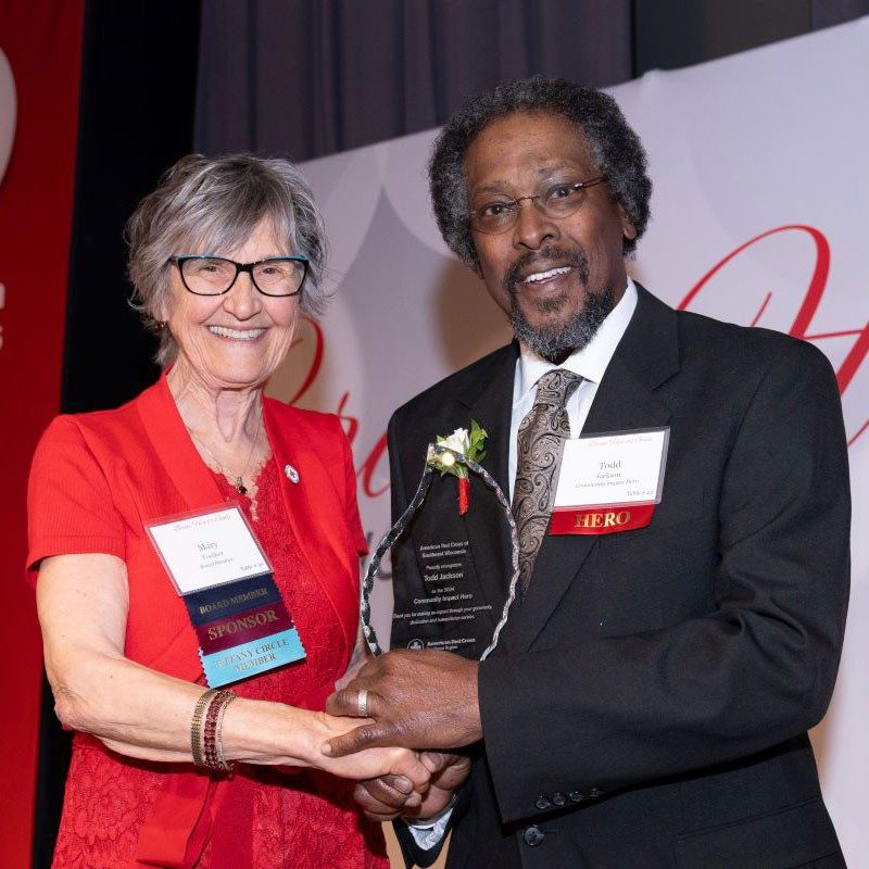 Red Cross employee and community member holding hero award at 2024 Brave Hearts Gala event.