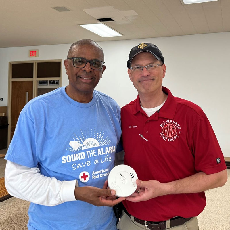 Two people with each of their hand holding a smoke alarm and smiling for picture.