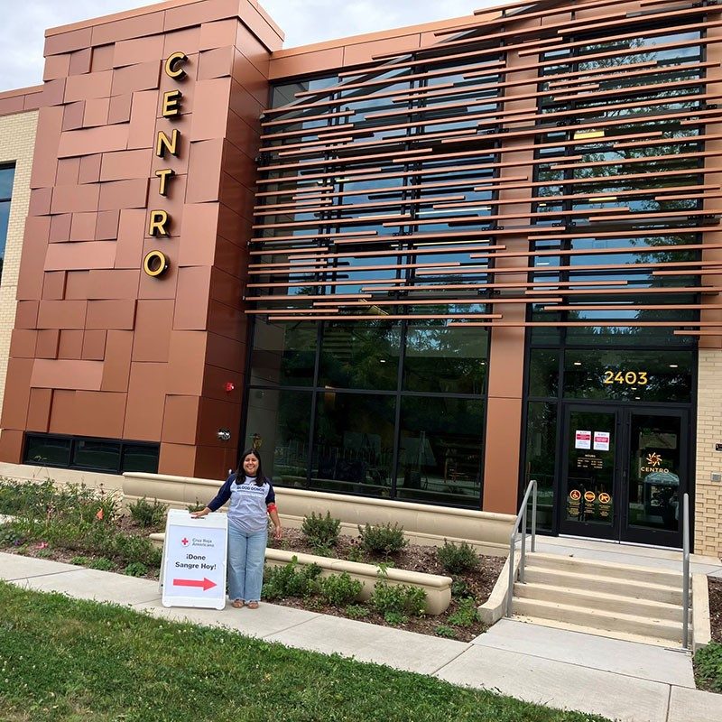 Person standing next to a blood donation sign by the entrance of the Centro Hispano building.