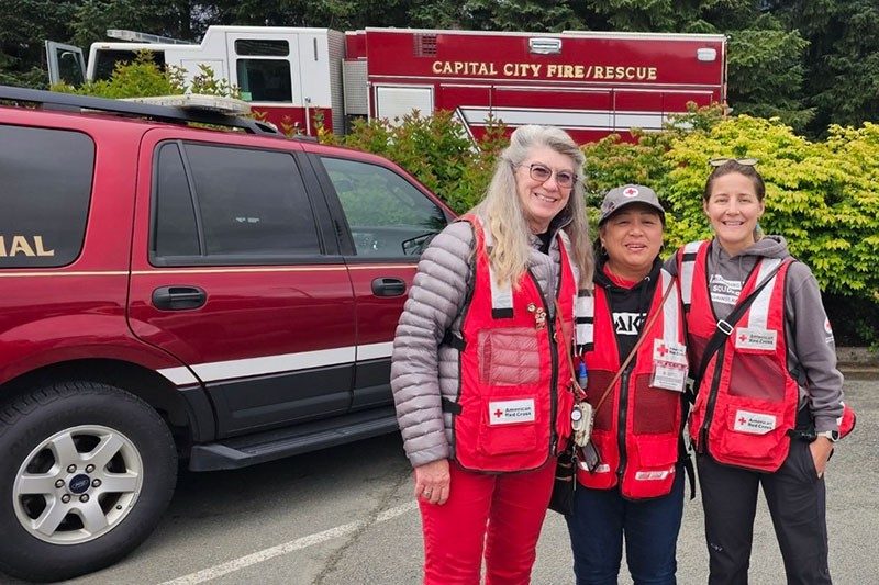 Three Red Cross volunteers in Red Cross vests with car and fire engine in the background.