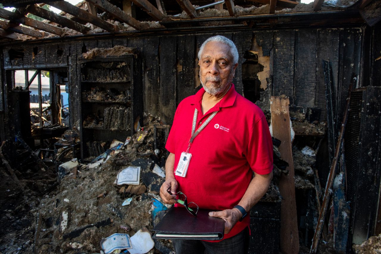 Red Cross volunteer with glasses and notebook in damaged home.