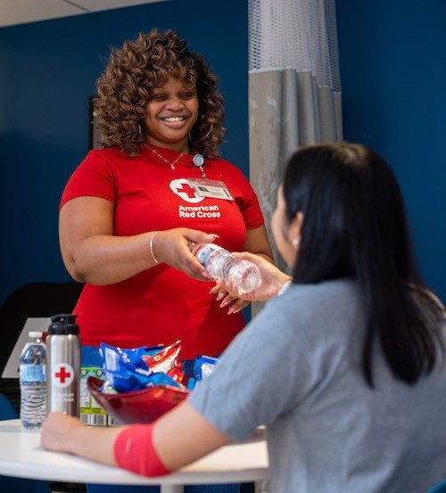 Red Cross volunteer handing water bottle to blood donor.