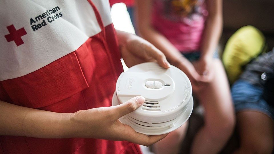 person in red cross vest holding two smoke alarms