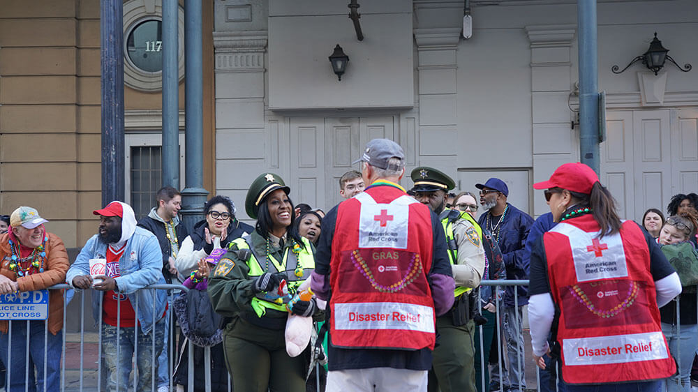 Red Cross volunteers wearing a Red Cross vests handing food to police officers at mardi gras parade.