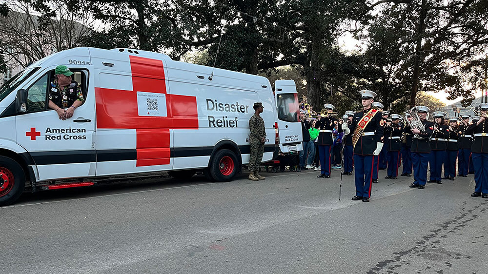 Military marching band in street next to a Red Cross van.