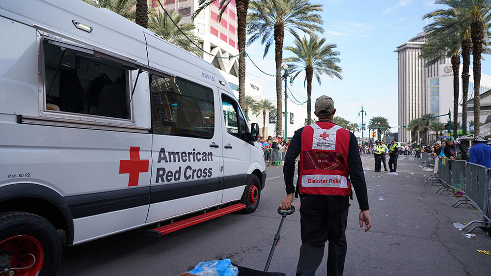Red Cross volunteer, next to Red Cross van, pulling wagon filled with water bottles towards police officers.