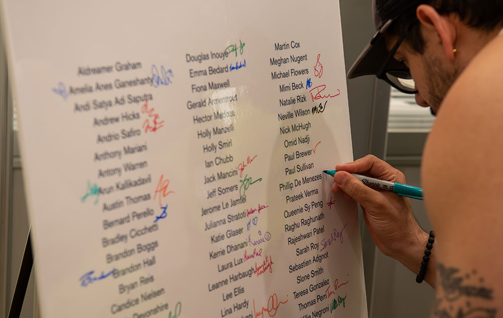 Whiteboard with list of names and person writing on it with a sharpie.