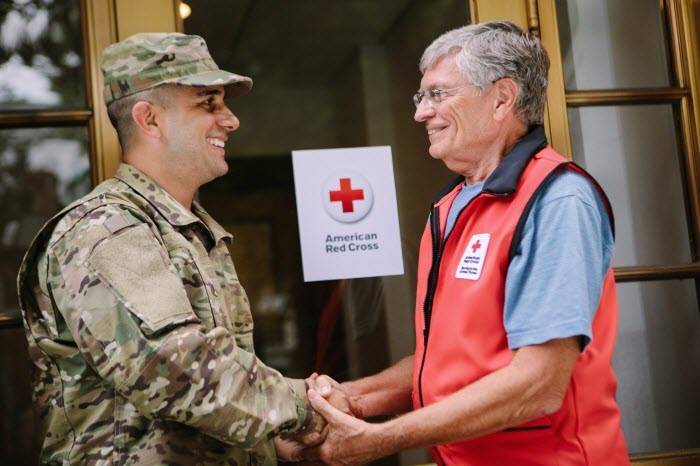 Red Cross volunteer and military service member shaking hands.