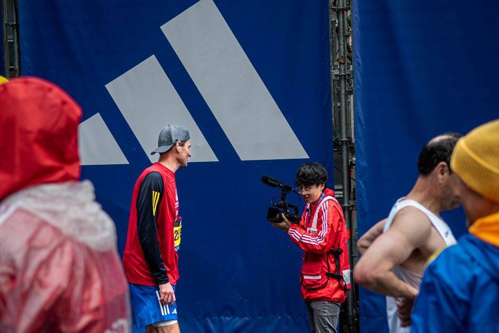 Noah Kreatz using camera to record marathon runner interview.
