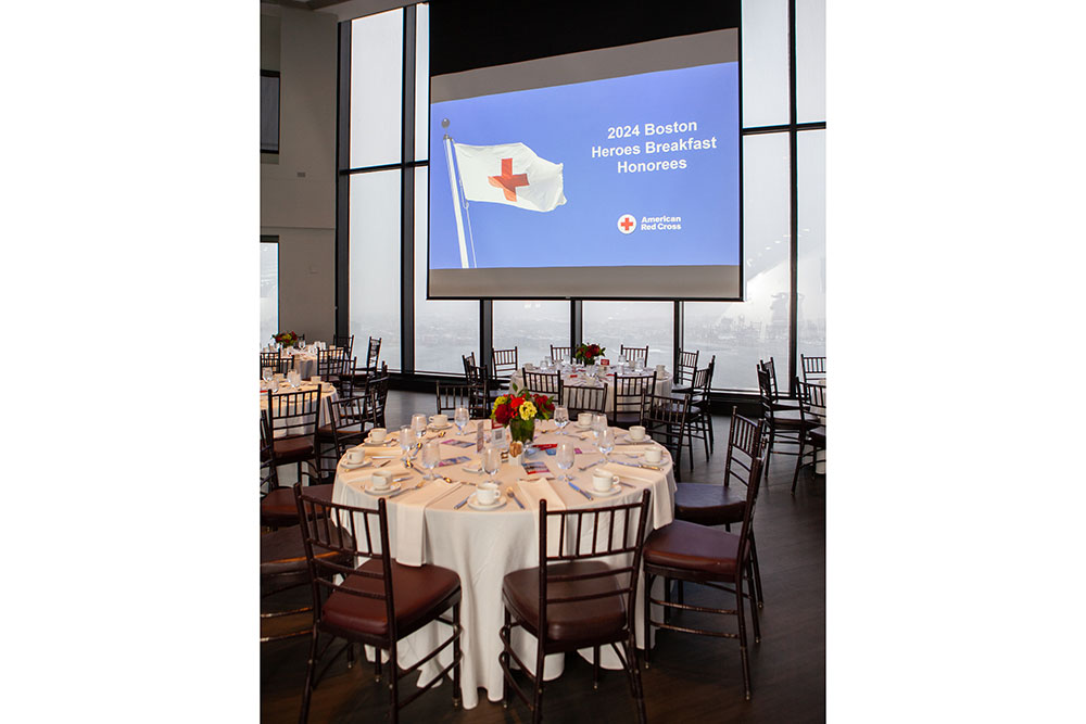 Dinner tables set with large projection screen hanging from ceiling in front of large windows