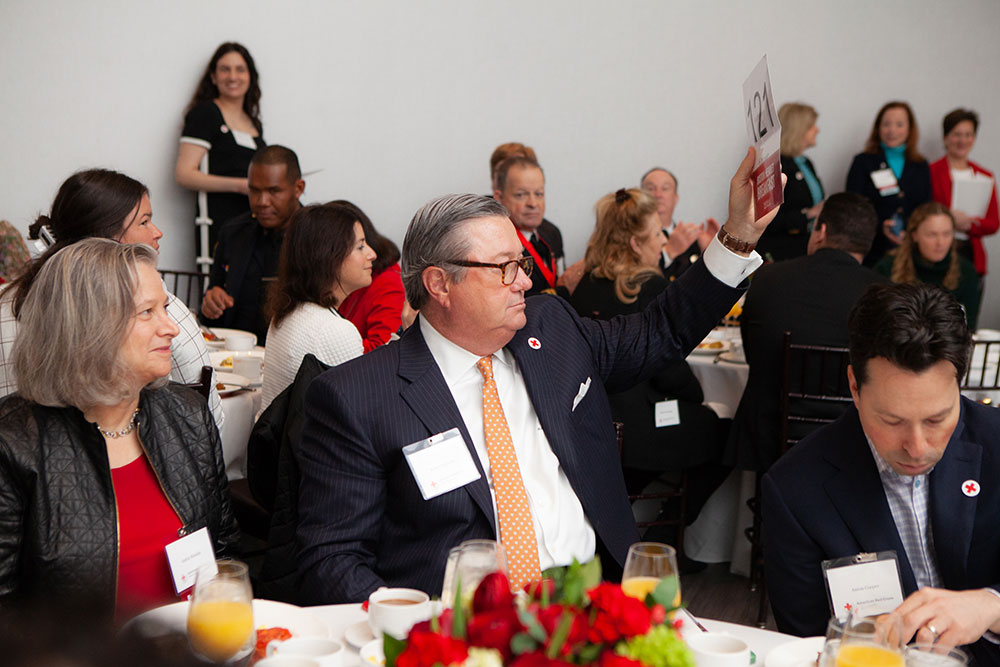 People sitting at event dinner tables with man holding up a card