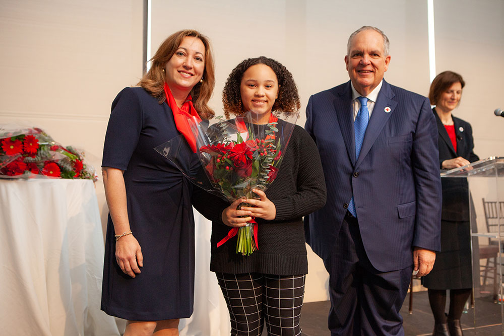 Youth hero Lilly Campbell wearing medal and holding a bouquet of flowers with two people on each side of her