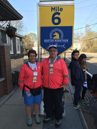 Two Red Cross volunteers standing next to a 6 mile marker for the Boston Marathon.