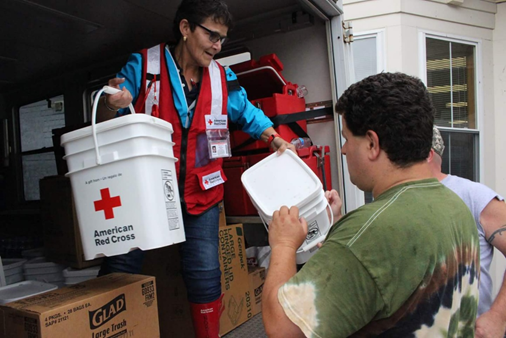Red Cross volunteer handing Red Cross 5 gallon buckets to residents.