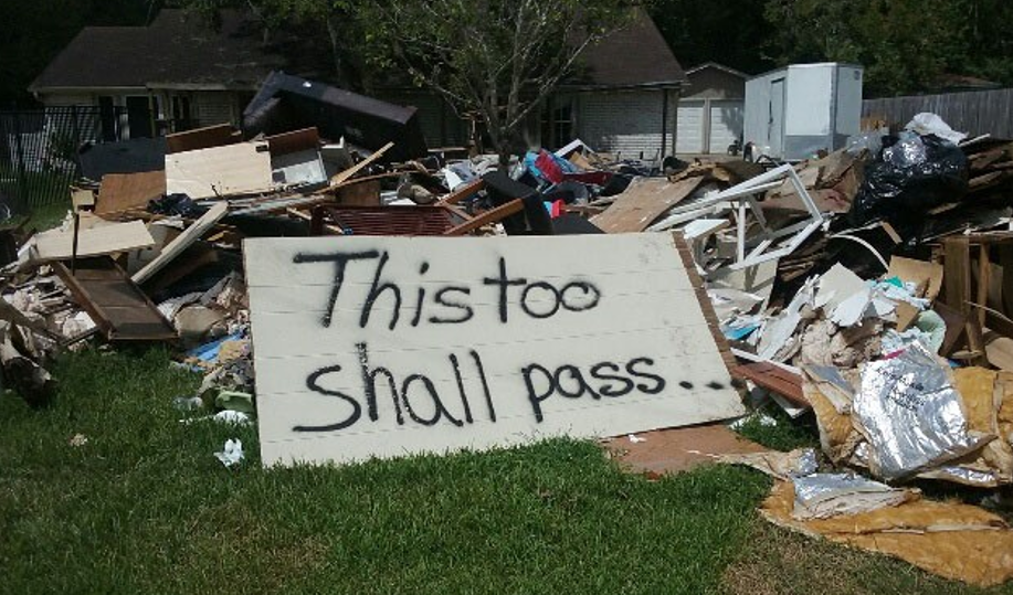 Lots of debris on a lawn with a sign that says "This too shall pass...".