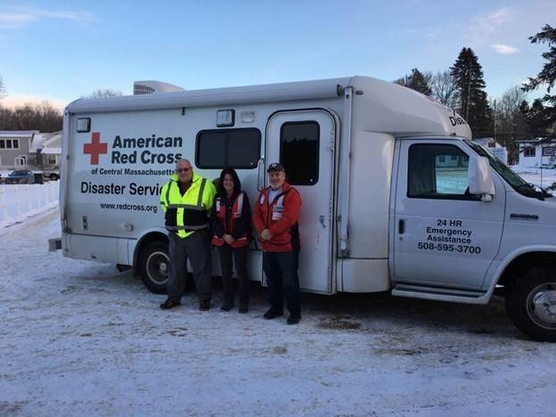 Three Red Cross volunteers standing in snow next to a Red Cross Distaster Service vehicle.