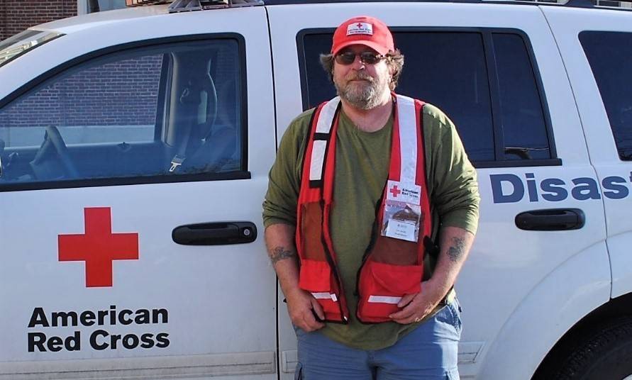 Keith McAuliffe wearing Red Cross hat and vest, standing next to a Red Cross vehicle.