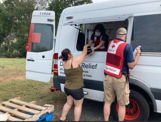 Red Cross volunteer handing food to person from a Red Cross disaster relief vehicle.