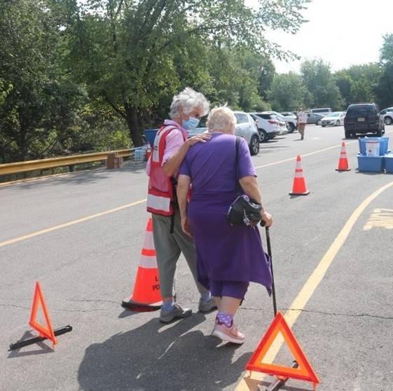 Red Cross volunteer helping person walking on street with a cane.