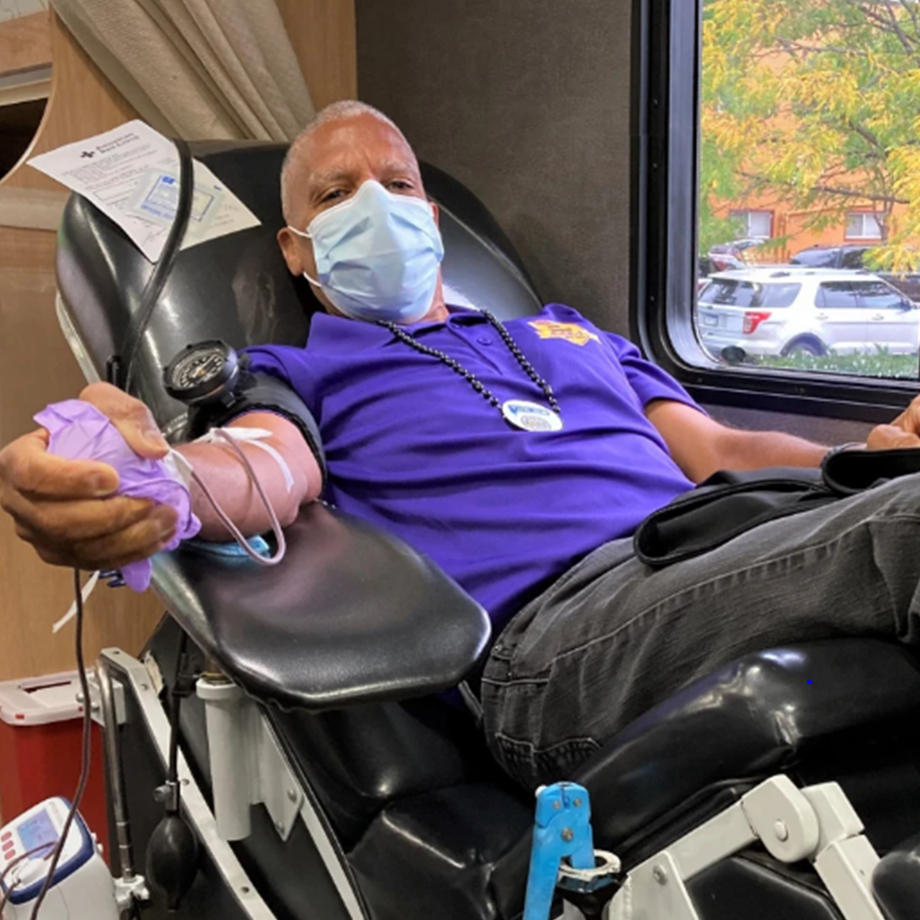Person wearing mask, sitting in chair, squeezing stress ball and donating blood.