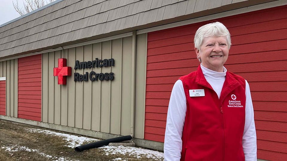 Red Cross volunteer Judi Leonard standing in front of a red cross building.