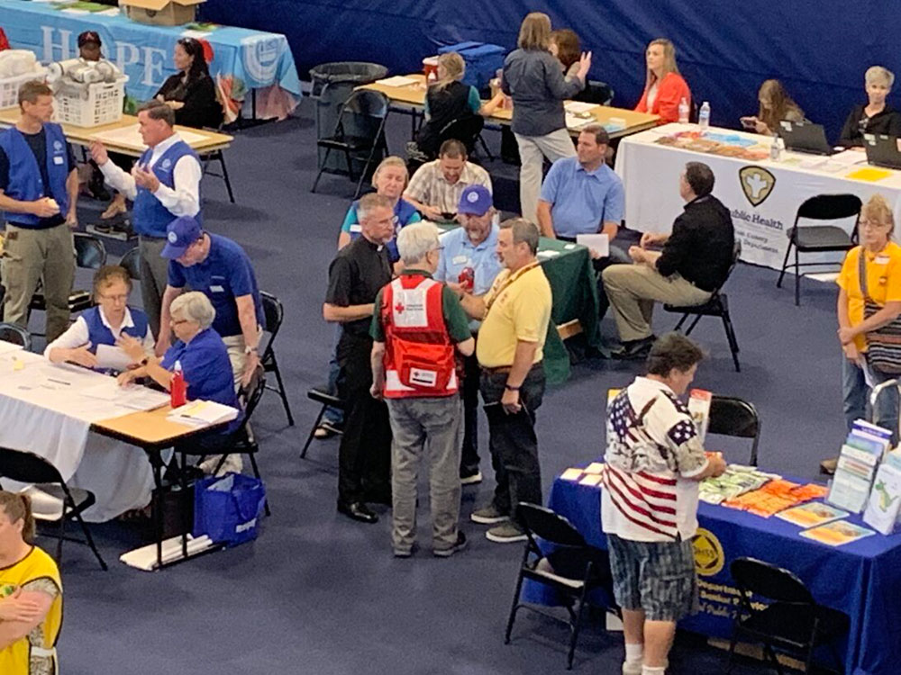Large room full of Red Cross volunteers, people, tables and chairs.
