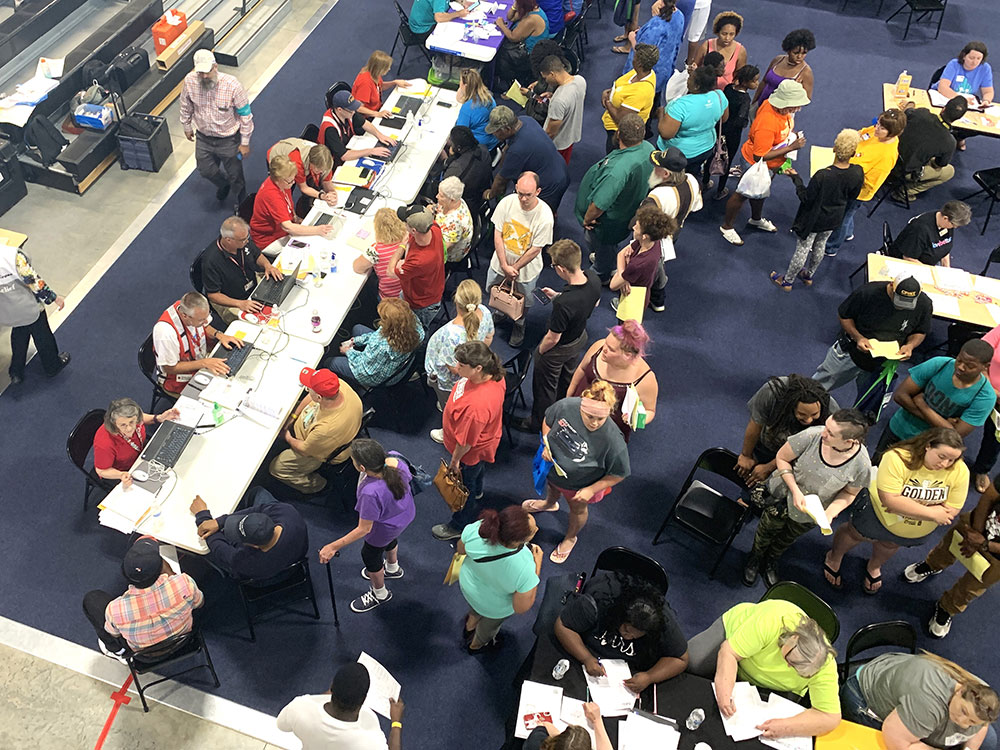 Large room full of Red Cross volunteers, people, tables and chairs.