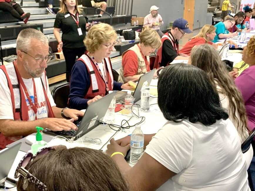 Red Cross volunteers and people sitting at tables getting help.