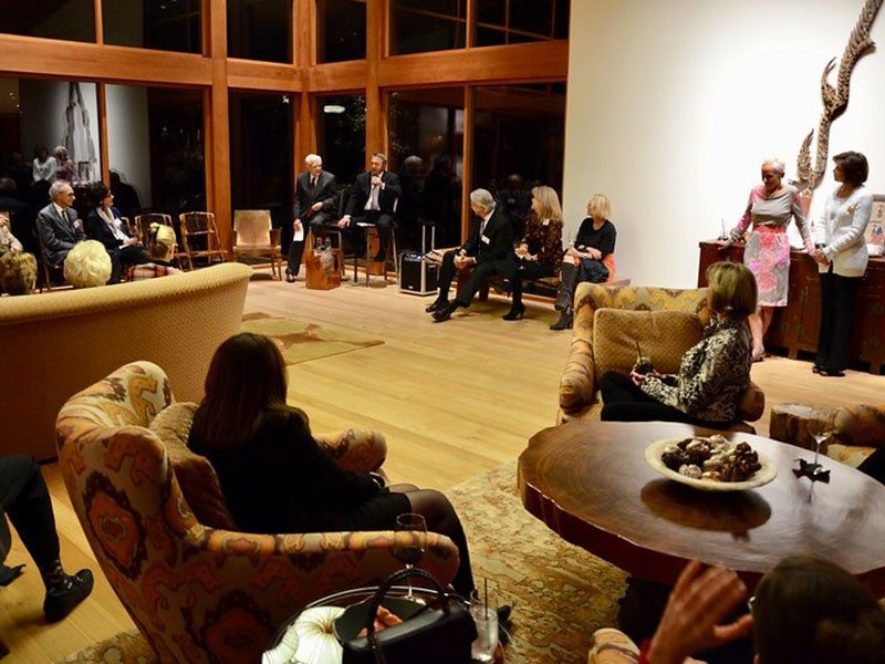 Group of people inside listening to person speaking on mic.