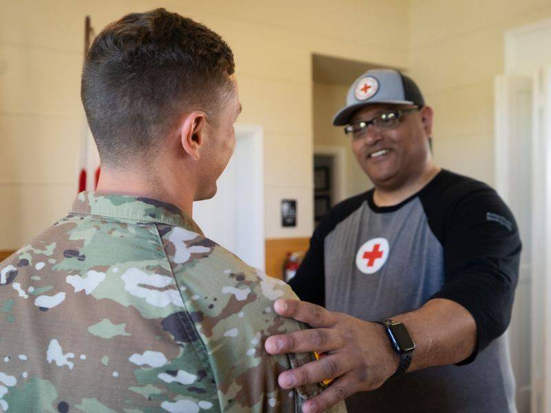 Red Cross volunteer smiling with hand on shoulder of military service member.