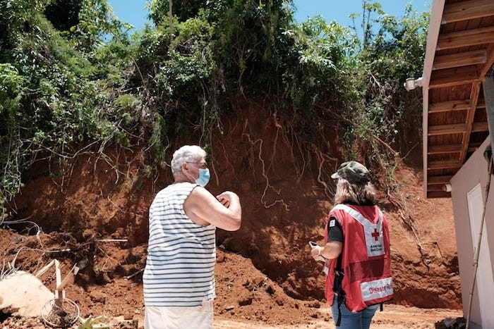 Voluntaria de la Cruz Roja junto a persona afectada por un desastre observa los daños en su hogar.