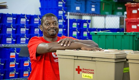 Voluntario posa junto a unos cajones con material de la Cruz Roja Americana.
