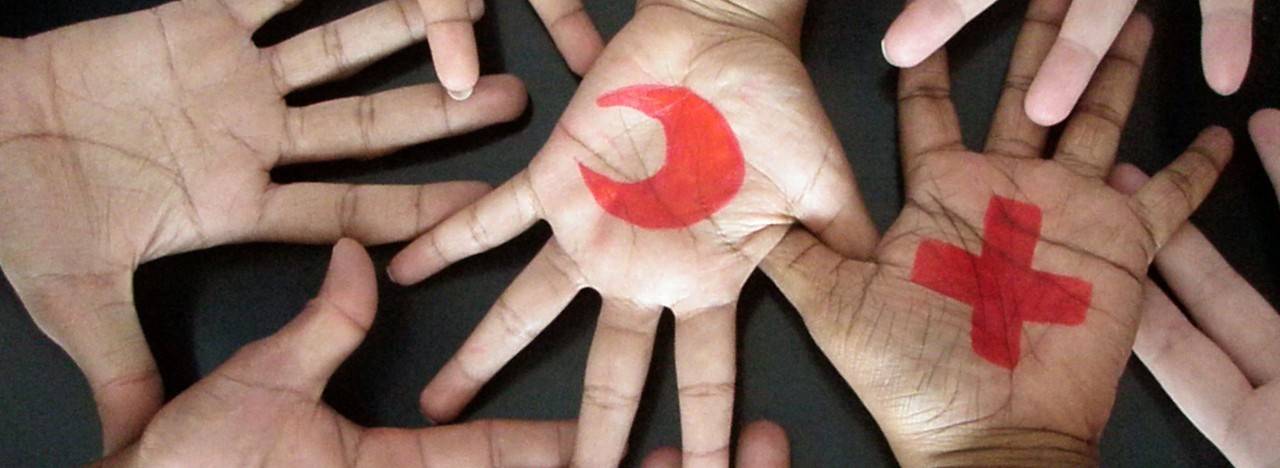 Multiple hands open with Red Cross and Red Crescent logos painted on them.